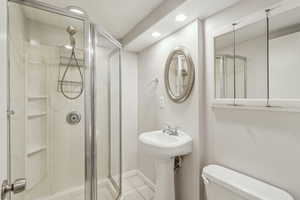 Full bath with a stall shower, baseboards, toilet, tile patterned floors, and recessed lighting