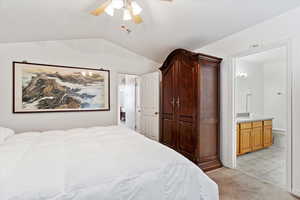 Bedroom featuring light carpet, ceiling fan, lofted ceiling, and ensuite bathroom