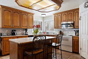 Kitchen featuring a kitchen island, stainless steel microwave, a breakfast bar, light countertops, and white range with electric cooktop