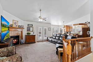 Living room featuring lofted ceiling, a ceiling fan, a tiled fireplace, and light colored carpet