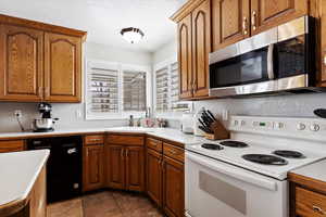 Kitchen with light countertops, stainless steel microwave, dishwasher, and white range with electric cooktop