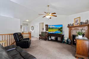 Living area featuring carpet floors, ceiling fan, vaulted ceiling, and a tile fireplace