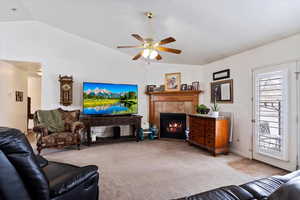 Living area featuring lofted ceiling, light carpet, a tile fireplace, and a ceiling fan