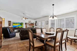 Dining room with lofted ceiling, a fireplace, a textured ceiling, and ceiling fan with notable chandelier