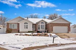 Ranch-style house with driveway, brick siding, an attached garage, fence, and stucco siding