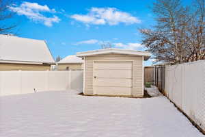 Snow covered garage featuring a detached garage and fence