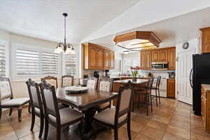 Dining area featuring a textured ceiling, vaulted ceiling, and a notable chandelier