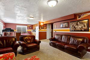 Living area featuring light colored carpet, a textured ceiling, and baseboards