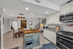 Kitchen featuring appliances with stainless steel finishes, light wood-type flooring, white cabinets, and visible vents