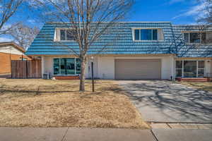 View of front of property featuring driveway, mansard roof, an attached garage, fence, and brick siding