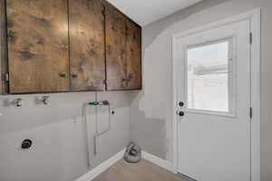 Clothes washing area with light wood finished floors, hookup for a washing machine, cabinet space, electric dryer hookup, and baseboards