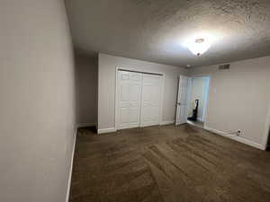 Unfurnished bedroom featuring baseboards, visible vents, dark colored carpet, a textured ceiling, and a closet