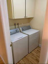 Washroom featuring baseboards, cabinet space, light wood finished floors, and washing machine and clothes dryer