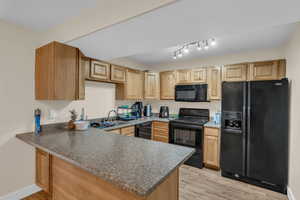 Kitchen featuring dark countertops, black appliances, a peninsula, and a sink