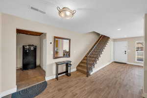 Entrance foyer with stairway, baseboards, visible vents, and wood finished floors