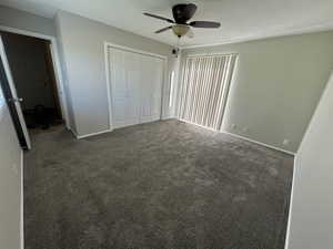 Unfurnished bedroom with baseboards, dark carpet, ceiling fan, and a closet