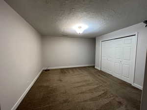 Unfurnished bedroom featuring a closet, dark carpet, a textured ceiling, and baseboards