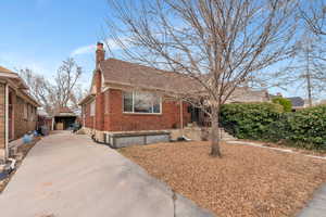 View of front facade featuring roof with shingles, a chimney, concrete driveway, and brick siding