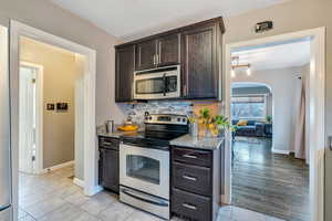 Kitchen with arched walkways, light stone countertops, stainless steel appliances, dark brown cabinets, and decorative backsplash