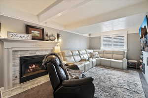 Living room with beamed ceiling, a tiled fireplace, and carpet floors