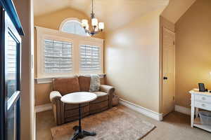 Master bedroom sitting area with lofted ceiling, light carpet, and an inviting chandelier