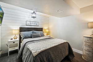 Bedroom with wood walls, a textured ceiling, and dark colored carpet