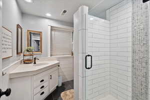 Basement bathroom featuring tile patterned flooring, vanity, a textured ceiling, and walk in shower