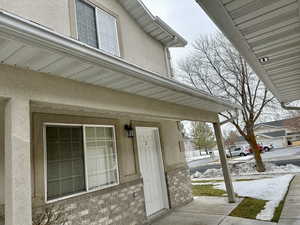 Snow covered property entrance featuring large front windows and covered front door adjacent to the garage