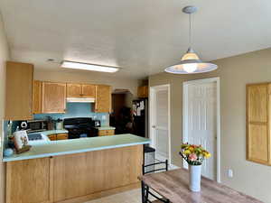 Cozy and efficient kitchen with black gas range, under cabinet range hood, a peninsula, and light countertops