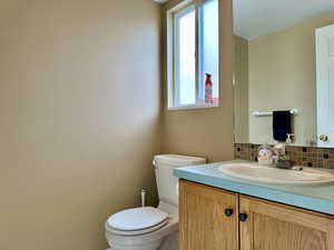 Half bathroom with toilet, backsplash, and vanity conveniently located on main floor