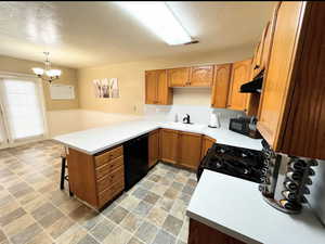 Spacious Kitchen with abundant cabinets, pendant lighting, a sink, under cabinet range hood, a peninsula, and black appliances