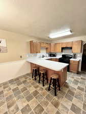 Kitchen featuring stone finish floor, a peninsula, light countertops, black appliances, and a kitchen bar