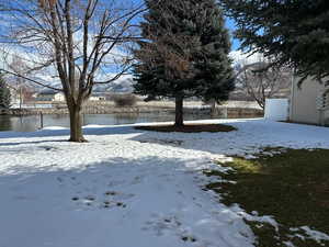 Yard layered in snow with a water view and fence