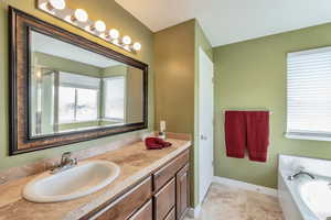 Bathroom featuring tile patterned floors, baseboards, a bath, and vanity