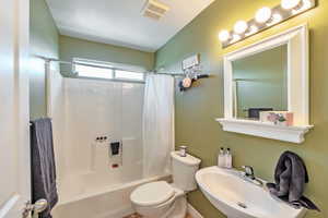 Bathroom featuring toilet, shower / bath combo, visible vents, and a sink