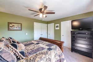 Bedroom with light carpet, ceiling fan, and two closets