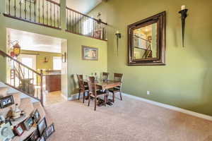 Dining room with light carpet, a high ceiling, visible vents, baseboards, and stairway