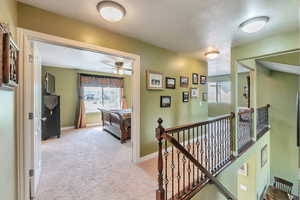 Corridor featuring baseboards, light colored carpet, and an upstairs landing