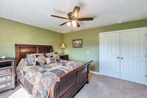 Bedroom with a closet, light carpet, ceiling fan, and baseboards