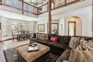 Living area featuring baseboards, arched walkways, wood finished floors, a high ceiling, and a notable chandelier