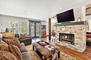 Living area with a textured ceiling, a stone fireplace, recessed lighting, wood finished floors, and french doors