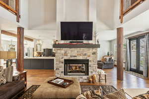 Living area with a towering ceiling, ornate columns, wood finished floors, and a stone fireplace