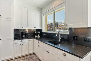 Kitchen with dark stone countertops, a sink, white cabinetry, and decorative backsplash