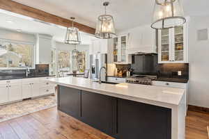 Kitchen featuring stove, a sink, white cabinets, custom exhaust hood, and decorative light fixtures