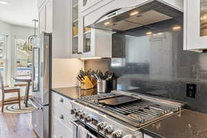 Kitchen with glass insert cabinets, dark countertops, high end appliances, and exhaust hood