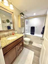 Full bathroom with shower / bath combination with glass door, visible vents, toilet, a textured ceiling, and wood finished floors