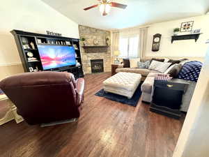 Living area with a fireplace, a ceiling fan, vaulted ceiling, and dark wood-style flooring