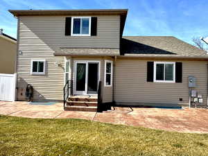 Rear view of property featuring a shingled roof, entry steps, a patio area, and a yard