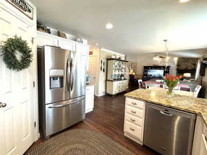 Kitchen with light stone counters, dark wood-style floors, appliances with stainless steel finishes, open floor plan, and white cabinetry