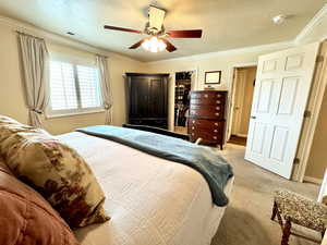 Carpeted primary bedroom featuring ornamental molding, visible vents, ceiling fan, and a textured ceiling